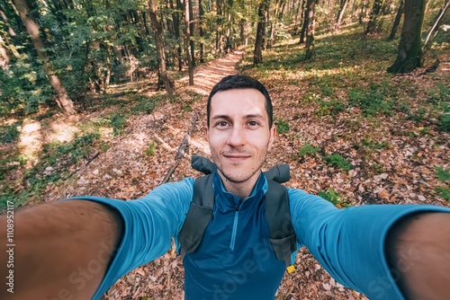 Young man on a solo hiking adventure, capturing a joyful selfie in a scenic forest park