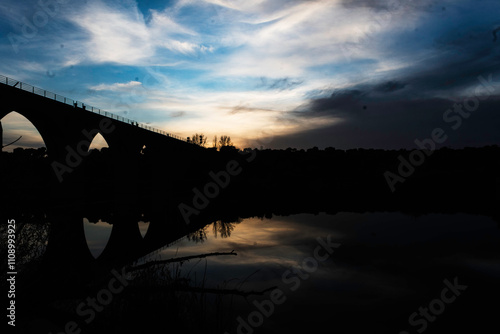 Silhouette of an Arched Bridge at Sunset Reflecting on Calm Waters in Fuentes Claras, Avila, CyL
