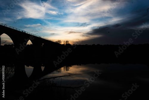 Silhouette of an Arched Bridge at Sunset Reflecting on Calm Waters in Fuentes Claras, Avila, CyL