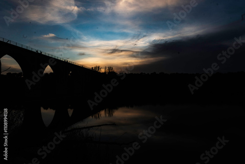 Silhouette of an Arched Bridge at Sunset Reflecting on Calm Waters in Fuentes Claras, Avila, CyL