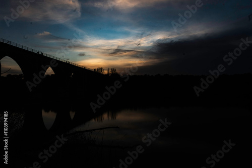 Silhouette of an Arched Bridge at Sunset Reflecting on Calm Waters in Fuentes Claras, Avila, CyL