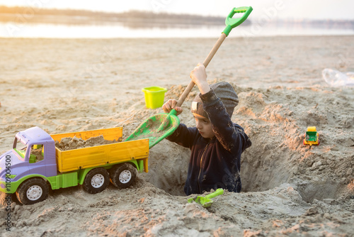 A child playing on the beach with a toy truck and shovel, digging a hole in the sand. The scene captures the joy and creativity of outdoor playtime by the water.