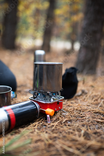 A man prepares a hot drink on a gas stove in a metal cup. A metal thermos. In the forest.