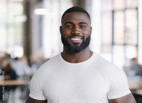 A smiling man with a beard stands confidently in a bright, modern workspace, exuding a friendly and approachable vibe.