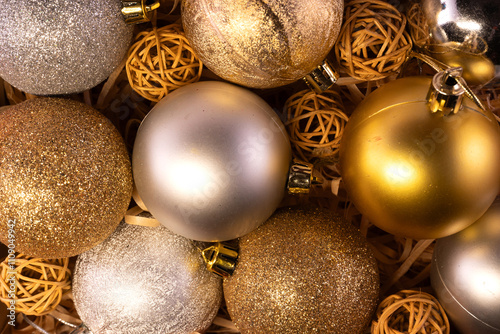 A festive arrangement of shiny metallic Christmas baubles in gold, silver, and bronze hues, set against a backdrop of decorative wicker balls. photo