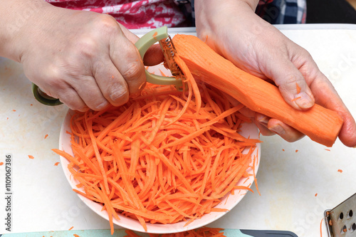 A woman cuts carrots into thin strips using a vegetable knife.