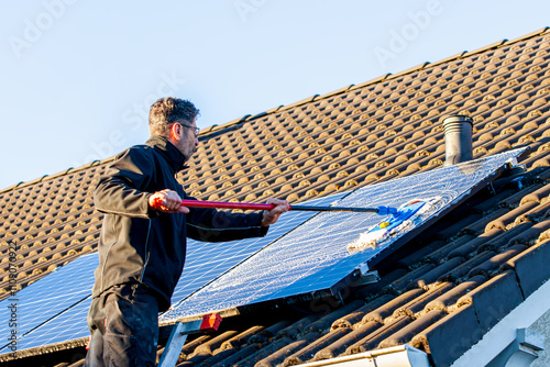 man holding mop cleaning solar panels. cleaning of solar modules with water. close-up of solar panels on the roof in winter. Mop cleaning. Washing of Solar modules in season photo