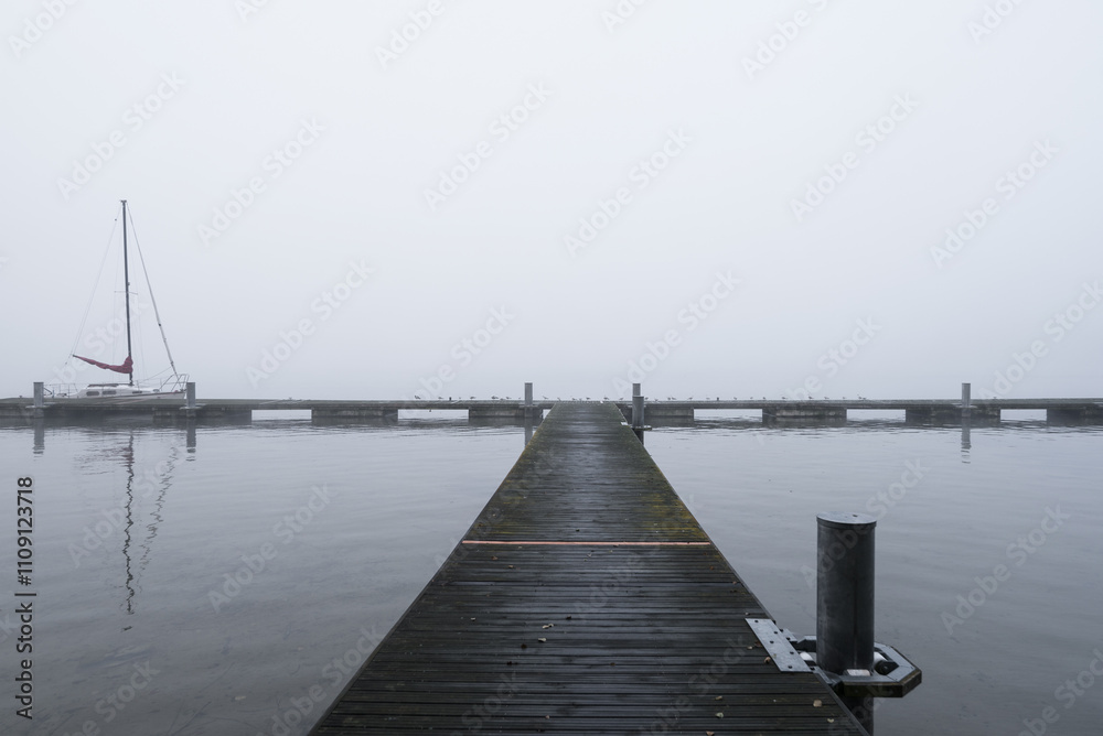 Obraz premium LANDSCAPE BY THE LAKE - A sailboat at the pier on a misty morning
