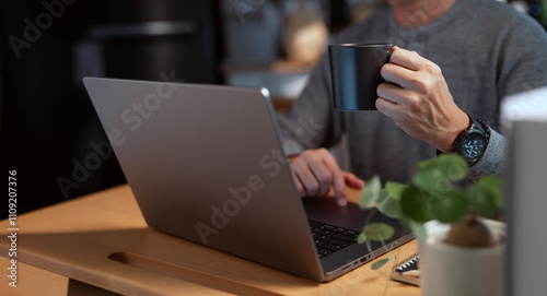 Fotografie Cropped shot of man holding coffee cup and using laptop compter at homeoffice