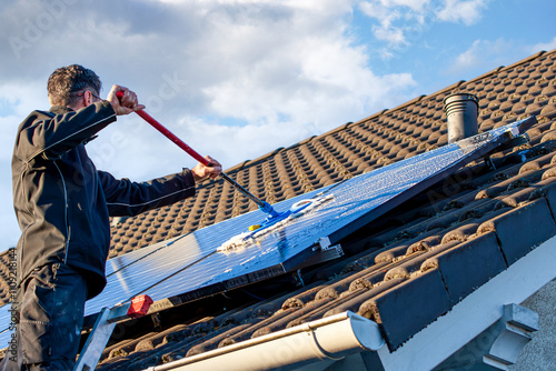 man holding mop cleaning solar panels. cleaning of solar modules with water. close-up of solar panels on the roof in winter. Mop cleaning. Washing of Solar modules in season photo