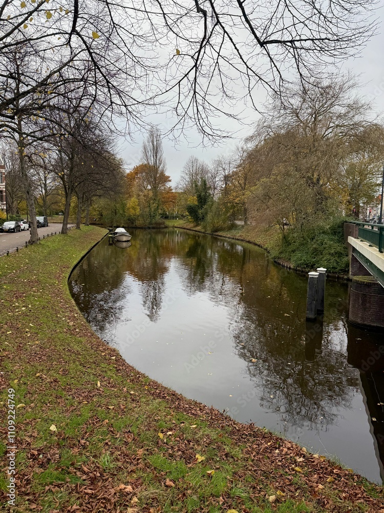 Obraz premium Beautiful view of canal with moored boat and colorful fallen leaves on autumn day