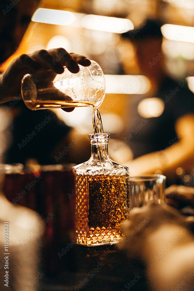 A bartender pours whiskey from a measuring glass into a decanter