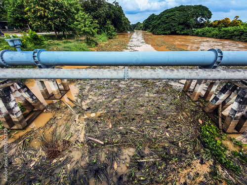 View of irrigation canal with weeds and debris flowing together with strong flowing dirty brown water due to soil and mud from forest after heavy rains and floods. La Nina crisis, Water pollution. photo