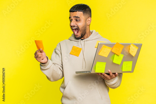 Exhausted freelancer Indian man with pasted sticker notes use laptop computer having concentration problem creative crisis. Nervous Arabian guy confused by big routine work loading yellow background photo