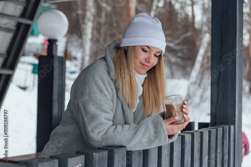 A beautiful young girl smiling and enjoying drinking coffee outdoors in a winter day.