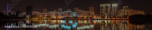 night city. widescreen panoramic view of a modern quarter with tall buildings on the coast of a large lake with electric lighting and reflection on the water surface. Minsk, Belarus. side view 25x5