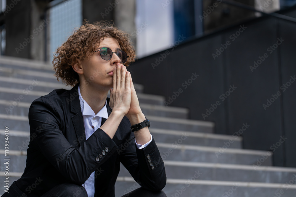 Fototapeta premium Nervous manager sitting on office steps. Pensive businessman in suit with hands joined making company decision. Successful CEO expert thinking silent break. Corporate leader pondering in downtown.