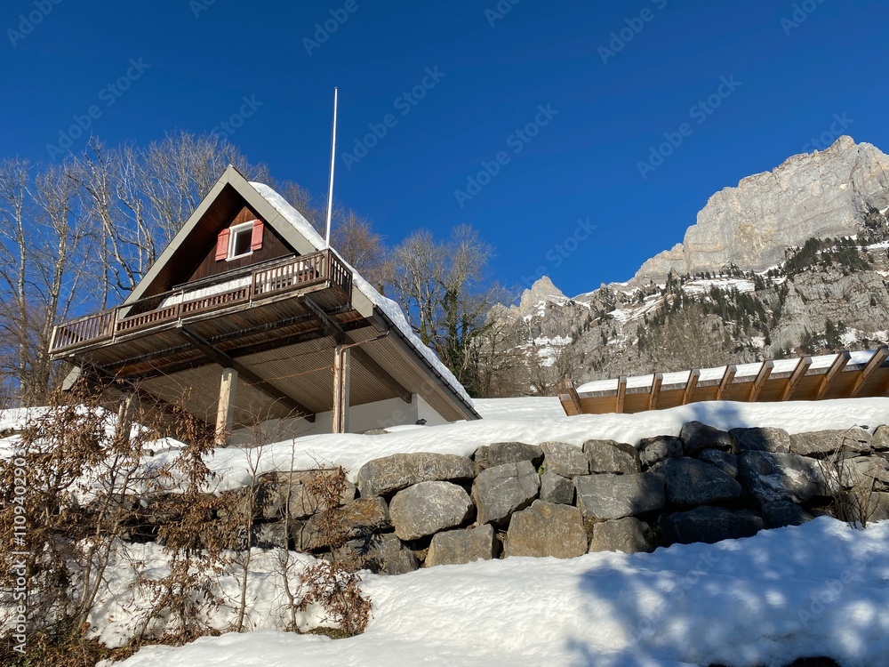 Fototapeta premium Old traditional swiss rural architecture and alpine livestock farms in the winter ambience over the Lake Walen or Lake Walenstadt (Walensee) and in Swiss Alps, Walenstadtberg - Switzerland (Schweiz)