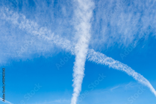 Contrail Exhaust Clouds from Jet Planes intersecting and dissipating in clear blue sky.  Chemtrails.
