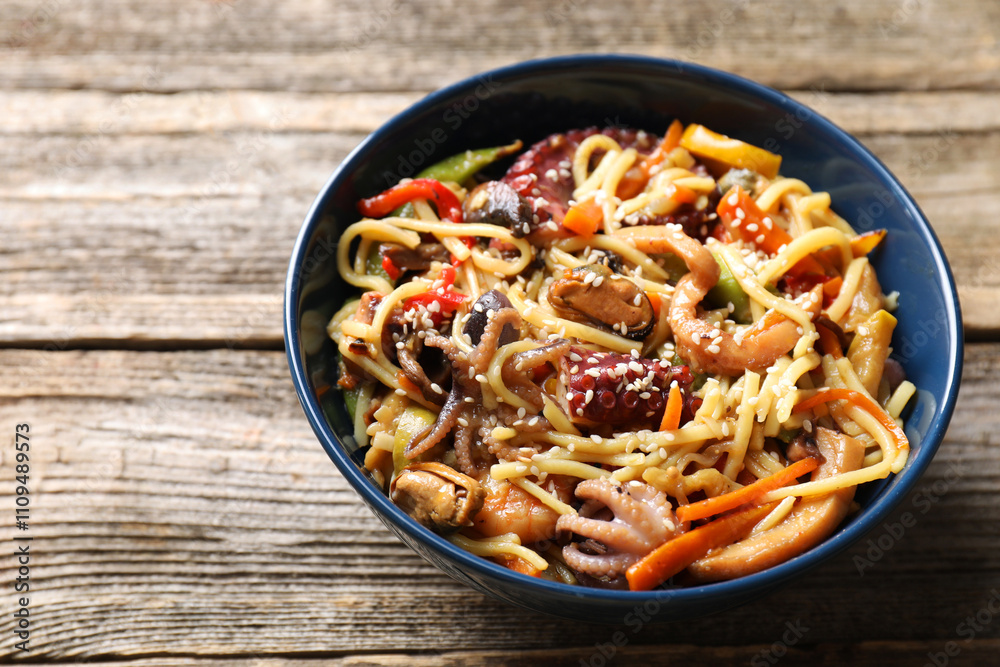 Stir-fry noodles with sea food and vegetables on wooden table, closeup. Space for text