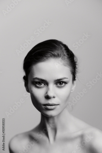 Elegant woman with a serious expression, showcasing natural beauty against a soft gray background. Minimalist portrait emphasizing features and emotions.