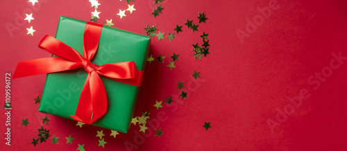 A beautifully wrapped green gift box with a vibrant red ribbon on a red background, perfect for Christmas or special occasions
