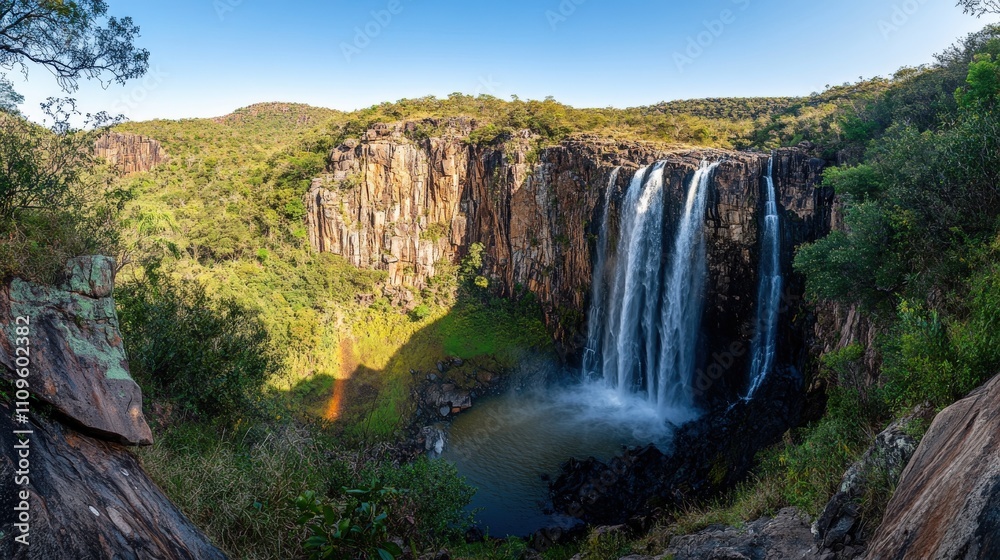 Fototapeta premium Dramatic Waterfall with Rainbow in Scenic Mountainous Backdrop at Golden Hour - Generative AI