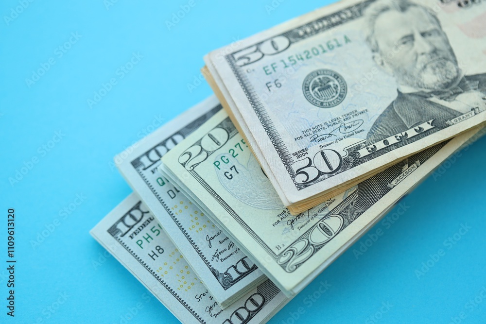 Big amount of hundred, fifty and twenty dollar bills in thick stack lies on bright blue color paper background Big amount of hundred, fifty and twenty dollar bills in thick stack lies on bright blue color paper background