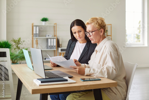 Colleagues working together during a business meeting in an office, using a laptop and documents. The teamwork reflects collaboration, negotiation, and efficient business practices.