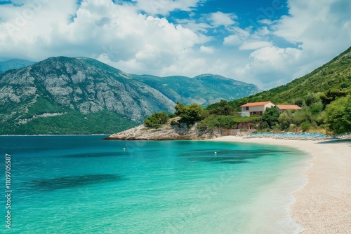 A beautiful beach with a house in the distance. The water is calm and clear. The sky is blue with some clouds