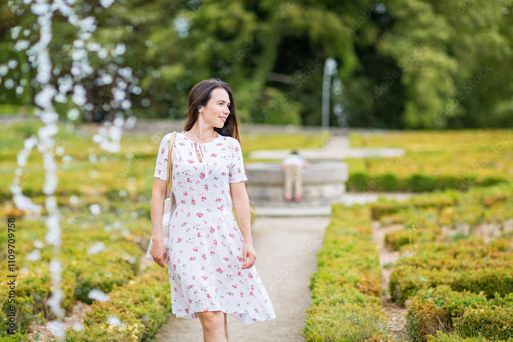 Lifestyle portrait of young pretty woman walking near fountain in a beautiful old park of a small French town Lifestyle portrait of young pretty woman walking near fountain in a beautiful old park of a small French town