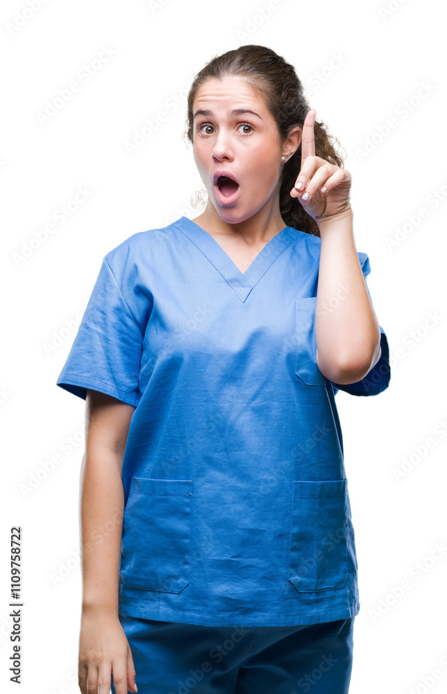 Young brunette doctor girl wearing nurse or surgeon uniform over isolated background pointing finger up with successful idea. Exited and happy. Number one. Young brunette doctor girl wearing nurse or surgeon uniform over isolated background pointing finger up with successful idea. Exited and happy. Number one.