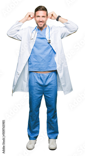 Handsome doctor man wearing medical uniform over isolated background Smiling pulling ears with fingers, funny gesture. Audition problem