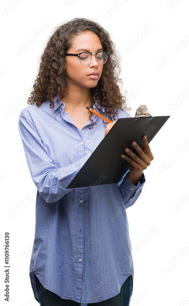 Young hispanic business woman holding clipboard with a confident expression on smart face thinking serious Young hispanic business woman holding clipboard with a confident expression on smart face thinking serious