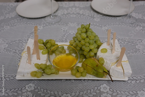 Canvastavla cheese with white mold Brie and grapes served with honey in a restaurant On a square plate with wooden skewers tasty delicacy
