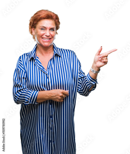 Atrractive senior caucasian redhead woman over isolated background with a big smile on face, pointing with hand and finger to the side looking at the camera. photo