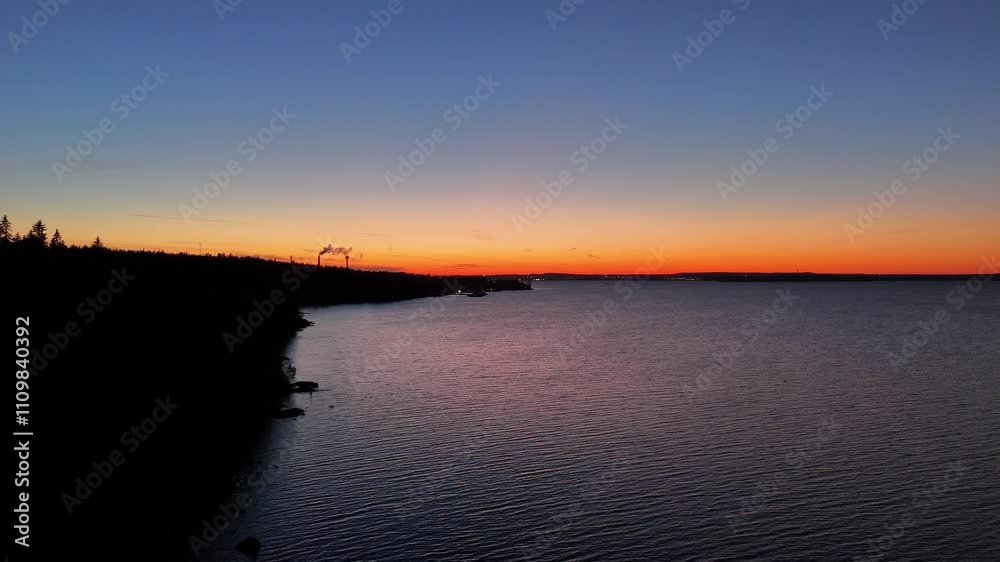 Flight over a lake with dark forested shore and the sunset colours in the horizon behind silhoutte of buildings of Tampere, Finland Flight over a lake with dark forested shore and the sunset colours in the horizon behind silhoutte of buildings of Tampere, Finland