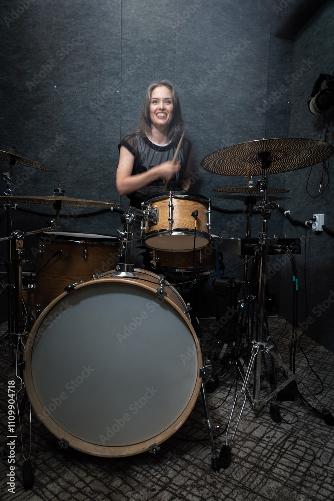 Fototapeta premium Smiling female drummer performing on drum set in professional soundproof studio. Vibrant scene emphasizes energy, creativity, and joy of live music creation, vertical image