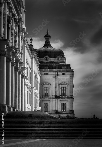 Dramatic black and white photography showcasing the grandeur of mafra national palace, highlighting its architectural details and imposing presence under a cloudy sky in lisbon, portugal