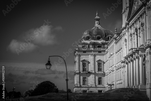 Dramatic black and white photo of the royal palace of mafra in portugal, with a vintage lamppost in front and intricate facade reaching towards the sky