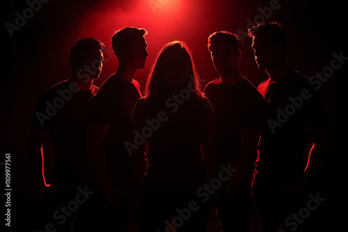 A group of people standing close together on music stage. red rim light.