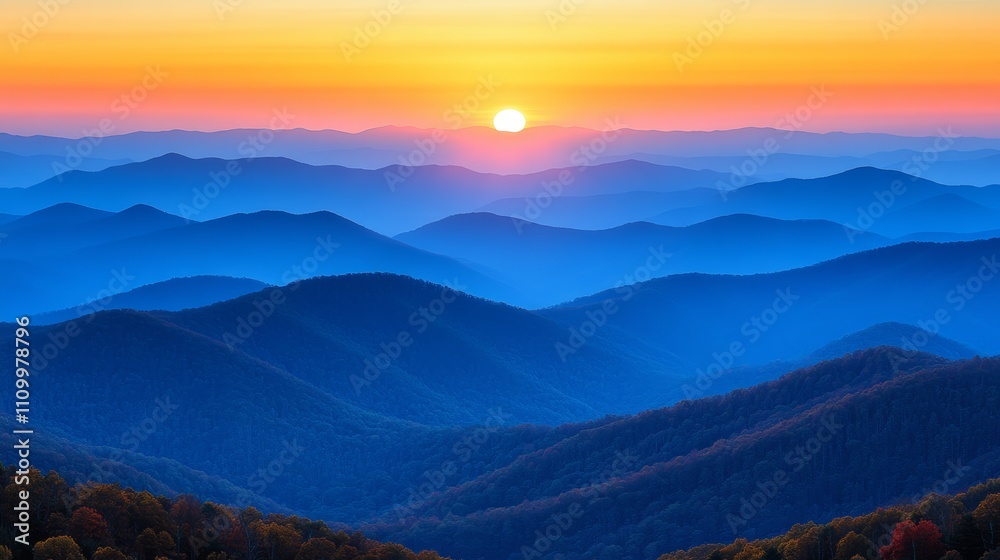 Fototapeta premium A vibrant sunset over a range of blue mountains, with a hazy golden sky above.
