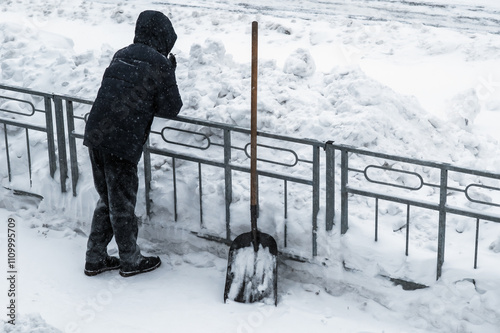 The janitor took a break from snow removal. The shovel is standing by the fence. Winter work after a snowfall. Rear view.