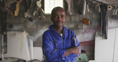 Obraz na plátně Portrait of a happy African male panel beater in a township workshop, holding a
