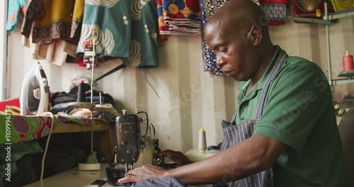 Obraz na płótnie Side view of an African male tailor in a township workshop, using a sewing machi