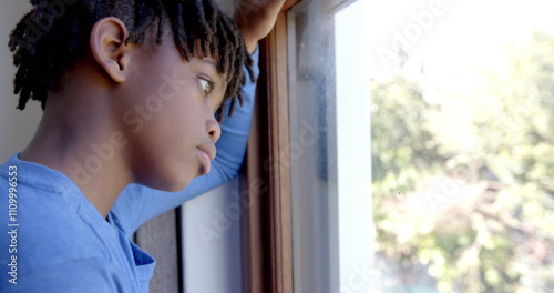 Free Download Thoughtful african american boy looking through window at home, slow motion - GFXLoad