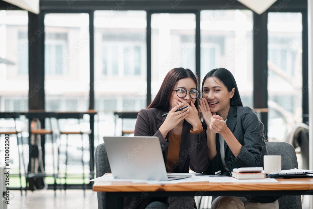 Fototapeta premium Two professional women laughing together in a contemporary office environment, showcasing teamwork and collaboration.