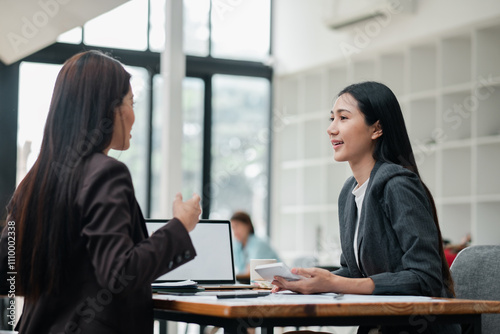 Two businesswomen engaged in a discussion at a modern office, showcasing teamwork and collaboration.