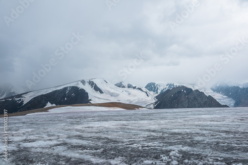 Wallpaper Mural Dramatic vast misty top view from ice pass to big glacier tongue among sharp rocks and large snow-capped mountains in rainy low clouds. Dark atmospheric mountain silhouettes in rain in gray cloudy sky Torontodigital.ca