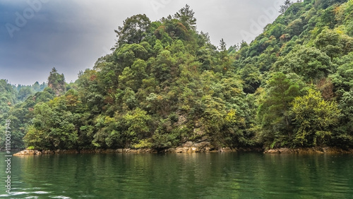 A calm emerald lake. Lush green vegetation grows on the coastal hills. Blue sky, clouds. China. Lake Baofeng. Wulingyuan